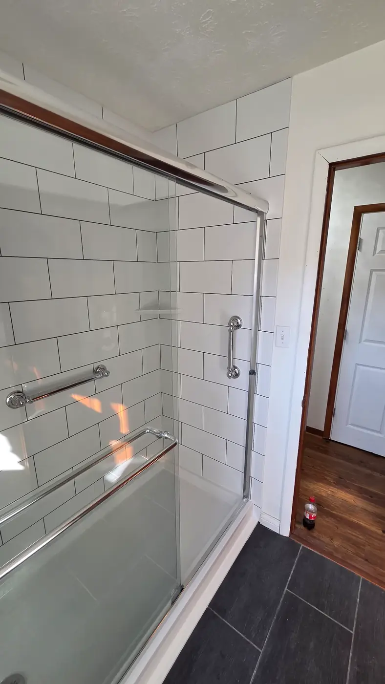 Framed sliding glass shower door beside a stained wood door in a Mason, OH bathroom remodel
