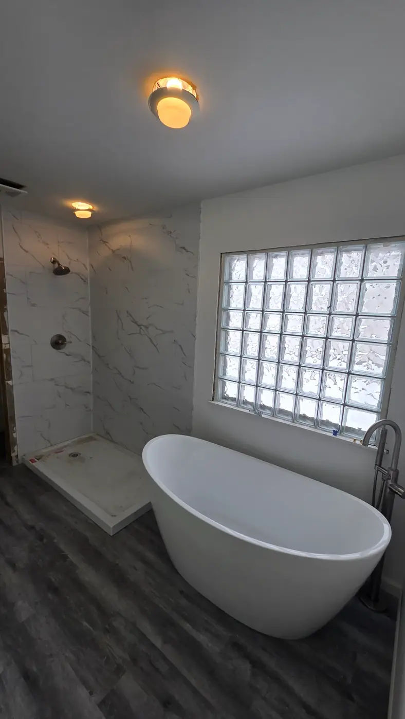 Freestanding soaking tub against marble-look tile and a glass block window in a Mason, OH bathroom remodel