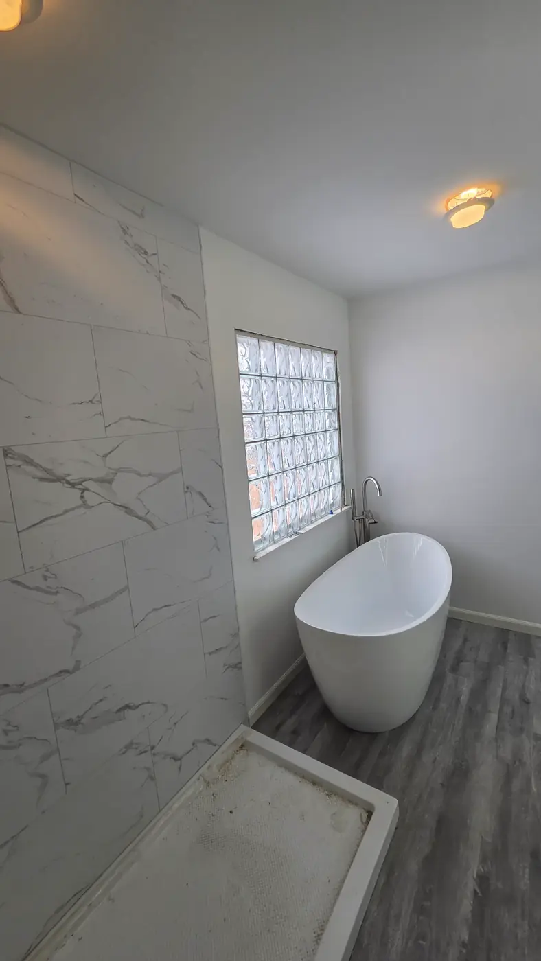 White freestanding tub with marble-look wall tile and gray plank flooring in Mason, OH